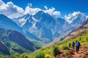 Hikers trekking through rocky paths in the Marrakech mountains, surrounded by rugged cliffs and dry terrain. In the distance, the towering peak of Mount Toubkal looms under clear blue skies, with scattered greenery along the trail.